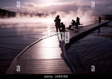 Besucher sind gegen die Sonne ab- und aufsteigenden Dampf im Grand Prismatic heißen Quellen im Yellowstone National Park, Wyoming, USA Stockfoto