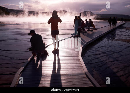 Besucher sind gegen die Sonne ab- und aufsteigenden Dampf im Grand Prismatic heißen Quellen im Yellowstone National Park, Wyoming, USA Stockfoto