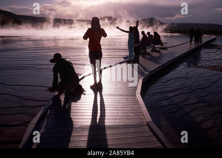 Besucher sind gegen die Sonne ab- und aufsteigenden Dampf im Grand Prismatic heißen Quellen im Yellowstone National Park, Wyoming, USA Stockfoto