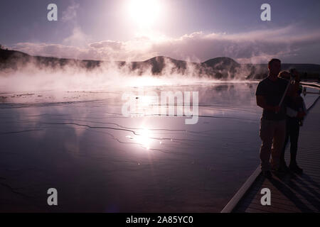 Besucher sind gegen die Sonne ab- und aufsteigenden Dampf im Grand Prismatic heißen Quellen im Yellowstone National Park, Wyoming, USA Stockfoto