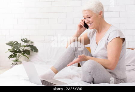 Positive senior Geschäftsfrau Arbeiten am Laptop und am Telefon sprechen Stockfoto