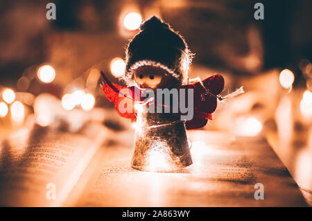 Holz Engel Weihnachten Girlande steht auf einem Buch, im Hintergrund ist eine LED-Kranz. Weihnachten Konzept. Stockfoto