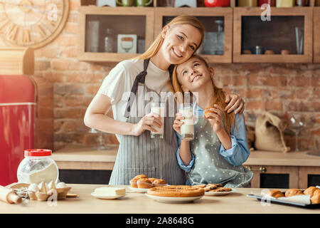 Glückliche Mutter und Tochter kleben beim Trinken von Milch nach dem Kochen Stockfoto