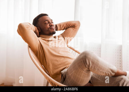 Schwarze Kerl entspannten Sitzen auf moderne Stuhl gegen Fenster Innen- Stockfoto