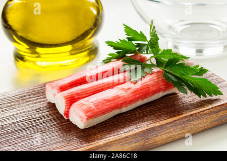 In der Nähe der Zeile von Surimi Crab Sticks auf einer hölzernen Schneidebrett in der Nähe von Olivenöl Glas Glas. Meeresfrüchte und Zutat für Salate. Das gesunde Essen. Stockfoto