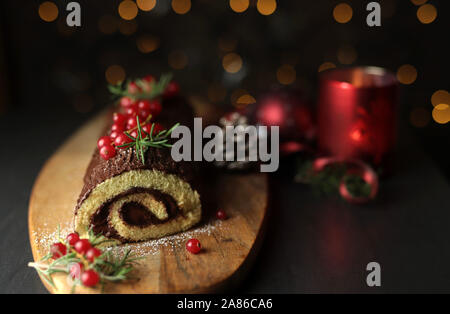 Schokolade Weihnachten Yule Log, Buche de Noel auf Holz Schneidebrett. Weihnachten Dekoration auf dunklem Hintergrund. Nahaufnahme Stockfoto
