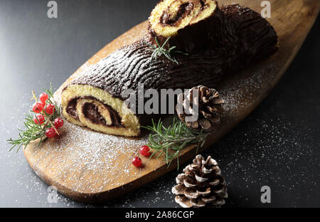 Schokolade Weihnachten Yule Log, Buche de Noel auf Holz Schneidebrett. Weihnachten Dekoration auf dunklem Hintergrund. Nahaufnahme Stockfoto