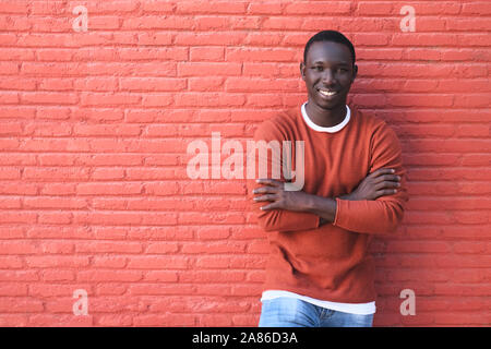 Portrait der Afrikanischen jungen Mann mit Kamera und lächelnd. Kopieren Sie Speicherplatz auf rote Wand im Hintergrund. Stockfoto