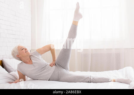 Sportliche ältere Dame, fit Übungen, auf dem Bett zu Hause liegen Stockfoto