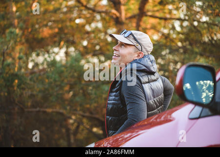 Ihnen gerne touristische Lean auf Auto zurück. Ein Mann lehnt sich auf der Motorhaube eines Autos. Der Blick von der Rückseite. SUV im Wald. Stockfoto