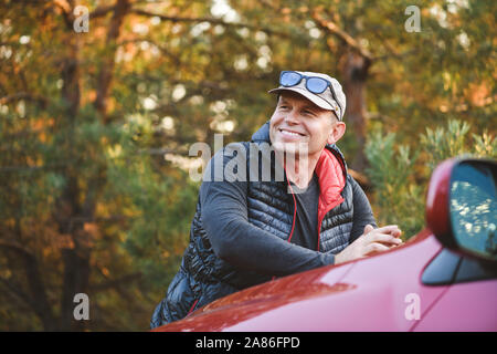 Lächelnd Mann lehnt sich auf der Motorhaube eines Autos. SUV im Wald. Stockfoto