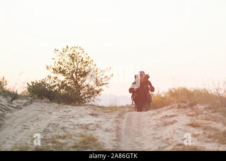 Männliche Wanderer mit riesigen Rucksack bewegen sich im Freien. Ein Mann Spaziergänge entlang der sandigen Weg. Stockfoto