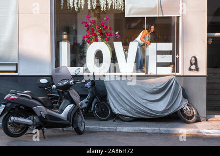 Konzept der Liebe. Vitrine mit einem Kapital LIEBE. Junge Mädchen schmückt Schaufenster, Motorrad auf der Straße in der Nähe der Fenster. Konzeptionelle Foto. Love Theme. Hintergrund im Rock Style. Mona Lisa stencil Stockfoto