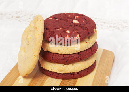 Stapel von weißer Schokolade Macadamianuss cookies und rotem Samt Cookies auf ein Schneidbrett, die wechselnden Farben. Diese Cookies sind ein Weihnachten und Stockfoto