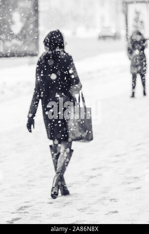 In einem städtischen Umfeld Blizzard. Silhouette eines eleganten schöne Frau in einen Mantel entlang einer eisigen verschneiten Pflaster. Abstrakte Blurry Winter Weath Stockfoto