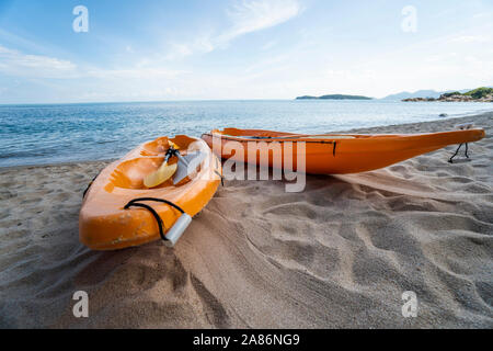 Zwei bunte orange Kajaks an einem Sandstrand für Paddler im sonnigen Tag bereit. Mehrere orange entspannende Boote auf dem Sand. Aktiven Tourismus und Wasser Stockfoto