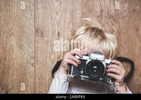 Junge, ein Foto mit einem Vintage Kamera zu Hause erlernen, wie Sie ein Bild das Kind hält die Kamera mit beiden Händen und nach Linse bei der v Stockfoto