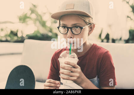 Trendige Junge trinkt ein Smoothie sitzen an der Bar im Freien. Mit Hut Getränke ein kaltes Getränk draußen im Garten jugendlich. Portrait von nachdenklich Teena Stockfoto