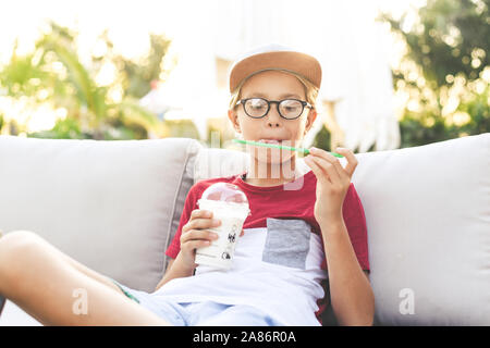 Trendige Junge trinkt ein Smoothie sitzen an der Bar im Freien. Mit Hut Getränke ein kaltes Getränk draußen im Garten jugendlich. Portrait von nachdenklich Teena Stockfoto