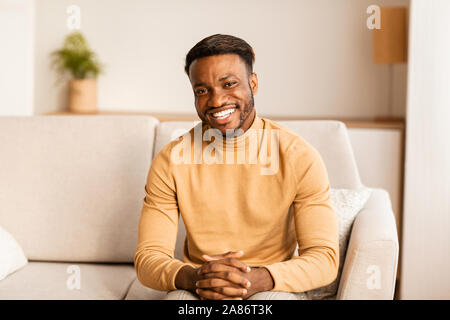 Positive Schwarzer Mann lächelnd an Kamera Sitzen auf der Couch Indoor Stockfoto