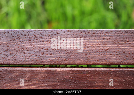 Holzbohlen durch Wassertropfen auf grünem Gras Hintergrund, regnerischen Wetter. Braun Holz Stockfoto