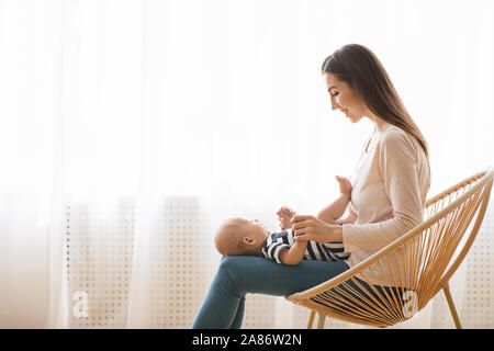 Junge Mutter sitzt im Korbstuhl mit Baby auf dem Schoß Stockfoto