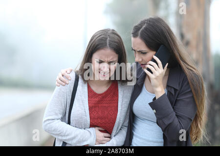 Vorderansicht Portrait eines Mädchens, das Bauchschmerzen und ein Freund ruft Hilfe Stockfoto