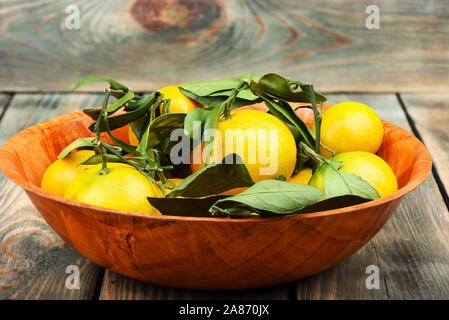 Mandarinen mit grünen Blättern. Tangerinen close-up in eine hölzerne Schüssel auf einem hölzernen Hintergrund. Im rustikalen Stil. Stockfoto