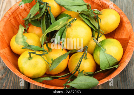 Mandarinen mit grünen Blättern. Closeup Mandarinen in eine hölzerne Schüssel auf einem hölzernen Hintergrund. Im rustikalen Stil. Stockfoto