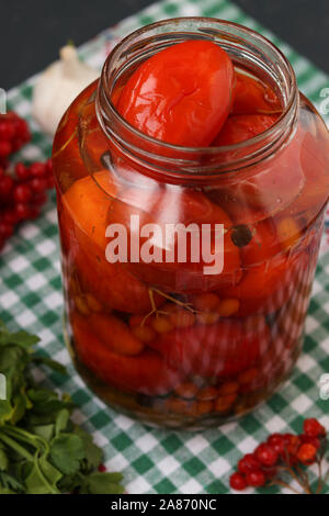 Marinierte Tomaten mit einem viburnum in einem offenen jar sind auf einem dunklen Hintergrund entfernt Stockfoto