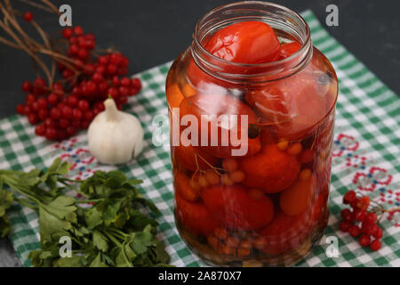 Marinierte Tomaten mit einem viburnum in einem offenen jar sind auf einem dunklen Hintergrund entfernt Stockfoto