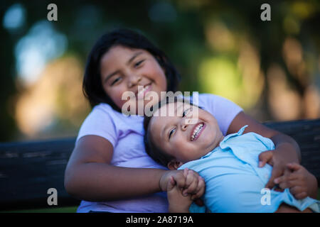 Kleiner Bruder genießen die Gesellschaft seiner Schwester wie er lacht mit einem freudigen Ausdruck und hält ihre Hand. Stockfoto