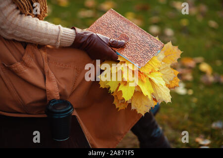 Hallo Herbst. Nahaufnahme auf trendige mittleren Alter Frau, Pullover, Rock, Handschuhe und Schal mit Notebook, gelbe Blätter und Tasse Kaffee, während er auf dem Stockfoto