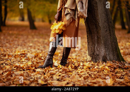 Hallo Herbst. Nahaufnahme auf trendige mittleren Alter Frau, Pullover, Rock, Handschuhe und Schal mit gelben Blätter im Herbst Park. Stockfoto