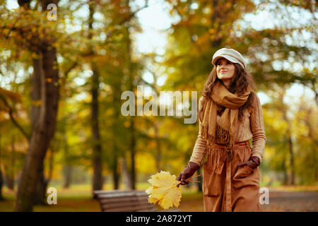 Hallo Herbst. lächelnd elegante 40-jährige Frau in die jacke, rock, hut, handschuhe und Schal mit gelben Blätter Wandern im Freien im Herbst Park. Stockfoto