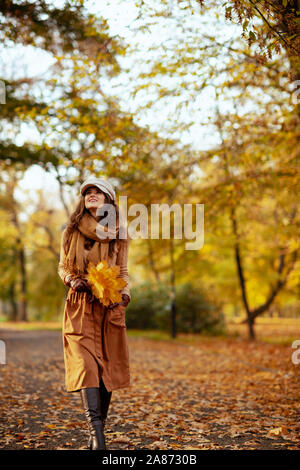 Hallo Herbst. Volle Länge Portrait von mittleren Alter Frau, Pullover, Rock, Mütze, Handschuhe und Schal mit gelben Blätter Wandern im Freien im Herbst Park Stockfoto