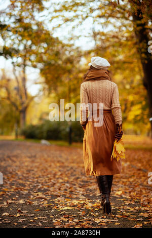 Hallo Herbst. Von hinten trendy Frau, Pullover, rock, hut, handschuhe und Schal mit gelben Blättern zu Fuß außerhalb im Herbst Park. Stockfoto