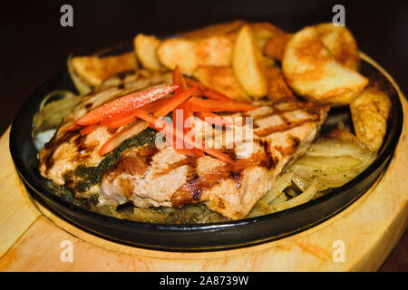 Große Schweinesteak mit Bratkartoffeln in einer gusseisernen Pfanne auf einem Tisch in einem Restaurant Stockfoto