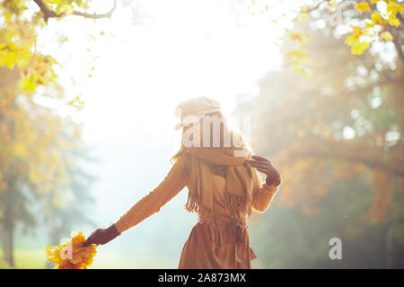 Hallo Herbst. lächelnd elegante 40 Jahre alte Frau in die jacke, rock, hut, handschuhe und Schal mit gelben Blättern im Freien im Herbst Park. Stockfoto