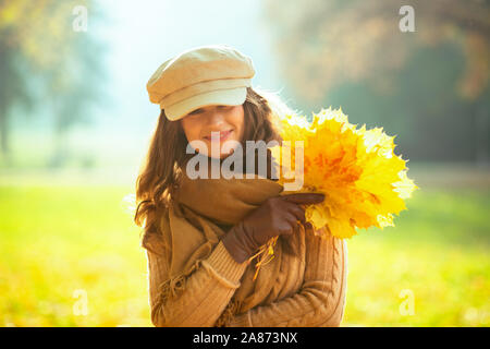 Hallo Herbst. Portrait von Happy stilvolle Frau, Pullover, Rock, Mütze, Handschuhe und Schal mit gelben Blättern im Freien im Herbst Park. Stockfoto