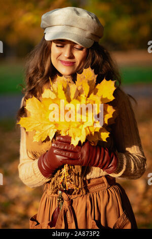 Hallo Herbst. Portrait von entspannt stilvolle Frau, Pullover, Rock, Mütze, Handschuhe und Schal mit gelben Blättern im Freien im Herbst Park. Stockfoto