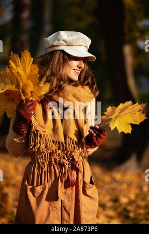 Hallo Herbst. lächelnd trendy Frau, Pullover, Rock, Mütze, Handschuhe und Schal außerhalb im Herbst park Sammlung gelbe Blätter. Stockfoto