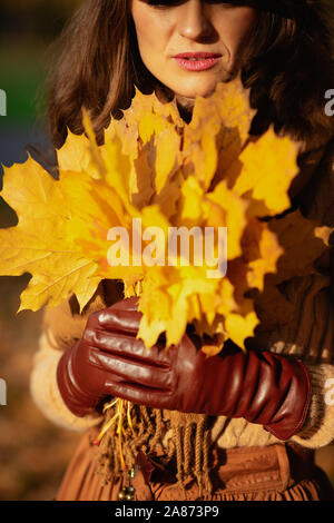Hallo Herbst. Nahaufnahme auf modernen Frau in die jacke, rock, hut, handschuhe und Schal mit gelben Blätter im Herbst Park. Stockfoto