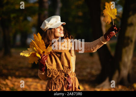 Hallo Herbst. Happy Elegant 40 Jahre alte Frau in die jacke, rock, hut, handschuhe und Schal außerhalb im Herbst Park am gelben Blatt suchen. Stockfoto