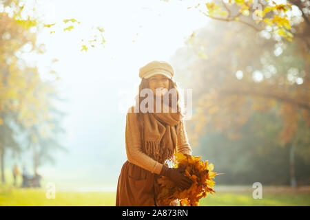 Hallo Herbst. Porträt der glückliche junge Frau, die in die jacke, rock, hut, handschuhe und Schal im Freien im Herbst park Holding einen Stapel der gelbe Blätter. Stockfoto