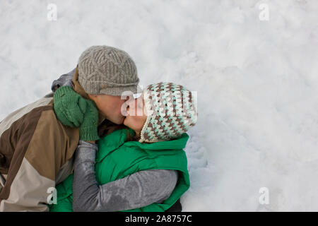 Junges Paar küssen beim Liegen im Schnee. Stockfoto