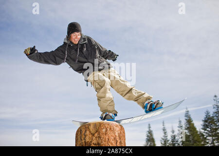 Snowboarder Balancieren auf einem Baumstumpf Stockfoto