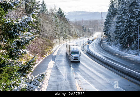 Weißes modernes Motorhaube gängigen professionellen Big Rig Semi Truck mit trockenen van Auflieger gehen auf den nassen gefährlich rutschigen eisigen Winter mit Schnee auf der Straße Stockfoto