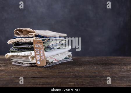 Stapel von Sachen liegen auf einem Holztisch. Baumwolle, Leinen in Pastellfarben Shirts, Fetzen Stoff, Schals. Stockfoto