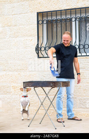 Pet-Liebe. Junge Glücklich macht BBQ mit Hund in den Hinterhof. Authentische Momente der Freude. Bärtiger Mann Grillen und Spielen mit Jack Russell Welpen. Hund auf den Hinterbeinen. Stockfoto